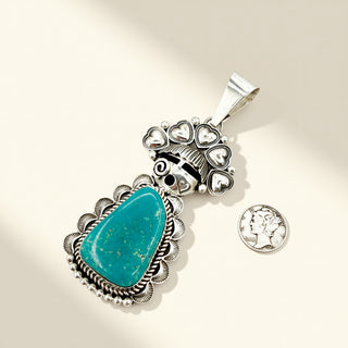 Silver pendant with turquoise stone and additional charms on a beige background