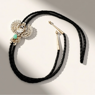 Black braided leather necklace with gold and silver pendants on a light gray background