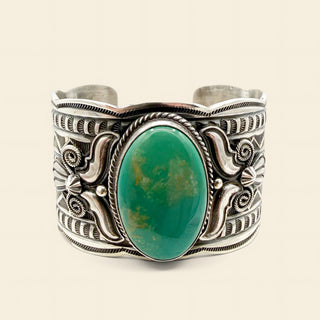 Silver cuff bracelet with a green stone on a beige background