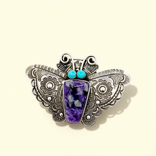 Butterfly-shaped ring with purple stone and turquoise gem on a beige background