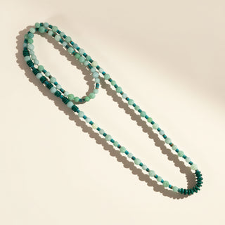 Long beaded necklace with green and blue beads on a beige background