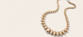 A  statement necklace made of large, glossy, teardrop-shaped beads, arranged in a U-shape on a light cream background.