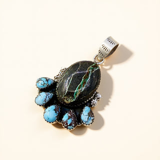 Jewelry pendant with turquoise stones and a dark stone on a beige background