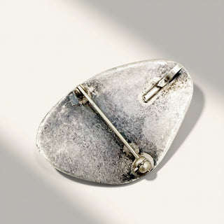 A silver-toned vintage pin with a textured, hammered finish and a barrette clasp, photographed on a light gray background with a soft shadow.
