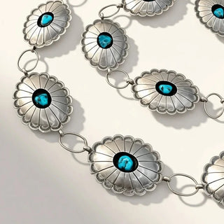 silver concho jewelry with turquoise stones on a chain against a beige background