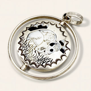 A sterling silver pendant featuring a detailed inlay and a silhouette of an animal, set within a circular silver frame with a bail at the top.