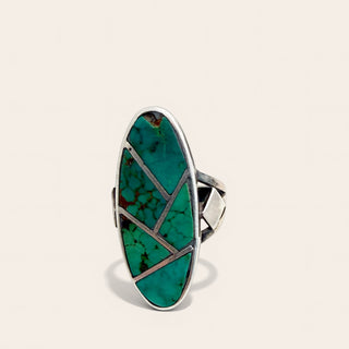A sterling silver ring featuring a large, vertically oriented oval inlay of vibrant green turquoise with natural matrix patterns and geometric silver line accents, set against a clean, light beige background.