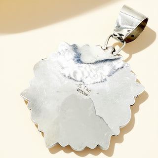 Silver pendant with scalloped edge on a beige background