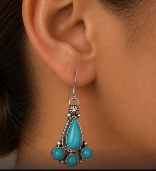 Turquoise teardrop earrings with silver accents worn by a person.
