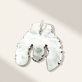 A silver pendant with a unique, organic silhouette and textured, hammered finish, shown on a warm beige background with soft diagonal shadows.