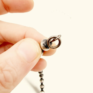 Hand holding a beaded necklace and 'Elgin' engraving on a plain background