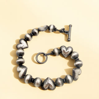 Silver heart-shaped beaded bracelet on a beige background