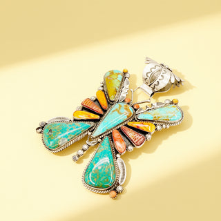 Silver pendant with green and orange stones on a beige background