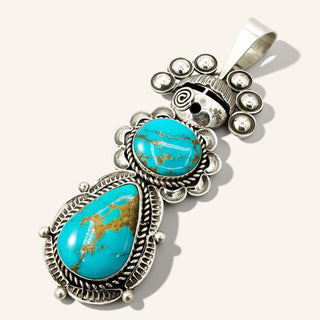 silver maiden pendant with two turquoise stones on a beige background