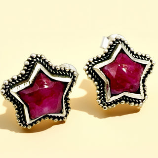 Star-shaped earrings with red gemstones and silver frames on a beige background