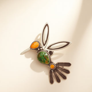 Hummingbird ring with turquoise and orange stones on a beige background