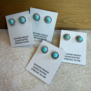 Turquoise stone earrings on white cards with text on a textured surface.