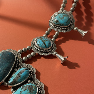 close up of necklace with turquoise stones and silver accents on a textured surface.