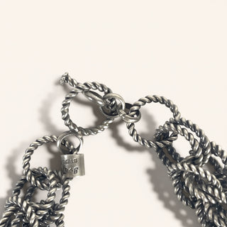 Close-up of a silver chain necklace with a tag on a light background