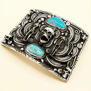 Decorative belt buckle with skull design and turquoise stones on a beige background