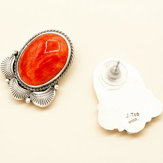 Silver earring with red stone and white stand on beige background