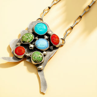 Multicolored gemstone pendant on a chain against a yellow background