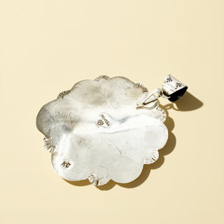 Silver pendant with a detailed design on a beige background