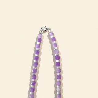 Beaded necklace with purple and silver beads on a beige background