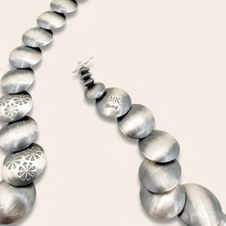 Silver beaded necklace with floral patterns on a light gray background