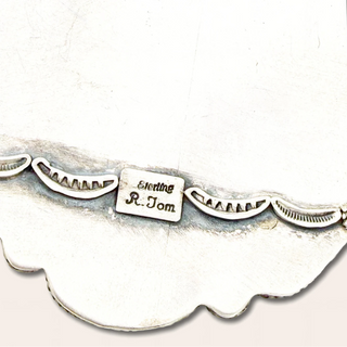 Decorative silver jewelry with scalloped edge and engraved text on a white background
