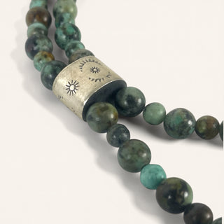 Beaded necklace with green and brown beads and a silver clasp on a white background