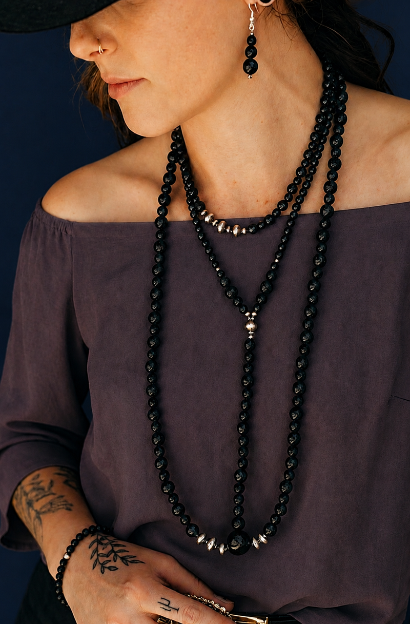 Woman wearing a long black beaded necklace against a dark background