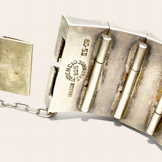 Close-up of a silver-toned bracelet clasp with engraved markings including  '925 Silver', showing the metal links and chain against a light neutral background.