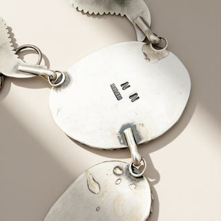 Close-up of a silver necklace with engraved initials on a beige background