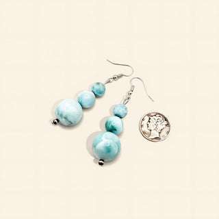 Turquoise beaded earrings with a silver pendant on a beige background
