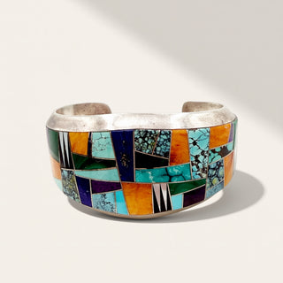 silver cuff with turquoise, green, blue and orange stones on a beige background