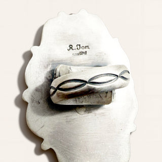A sterling silver ring with a textured, organic-shaped backing, featuring a band with a stylized infinity-like loop pattern. The inside of the backing is stamped with 'R.