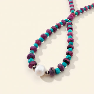 Necklace with purple and turquoise beads and a white pearl on a beige background