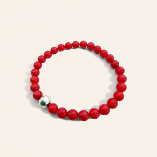 Red beaded bracelet with a silver charm on a light pink background