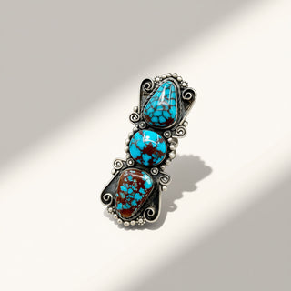 A silver-toned Southwestern-style ring featuring three stacked turquoise cabochons with brown matrix, set against a warm off-white background with soft diagonal shadows.