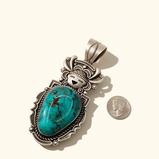 Turquoise stone pendant with silver detailing next to a penny for scale on a white background