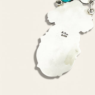 Silver jewelry 'R. Tom' branding on a light pink background