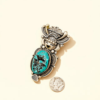 Jewelry ring with turquoise stone and silver accents next to a quarter for scale on a beige background