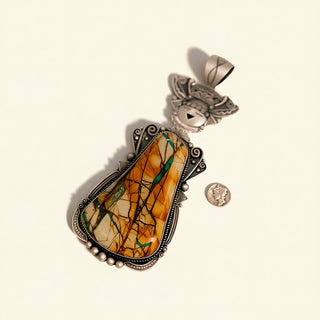 Jewelry pendant with a decorative stone and silver frame on a beige background