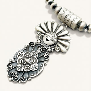 Silver necklace with intricate designs on a white background