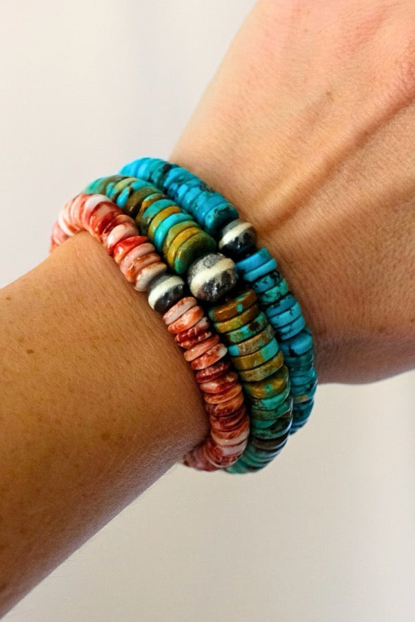 Hand wearing colorful beaded bracelets on a plain background