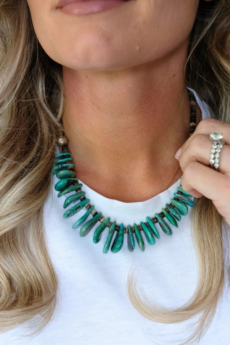 Close-up of a person wearing a green beaded necklace with a white top.