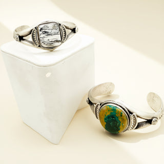 Two silver cuffs with intricate stones on a beige background