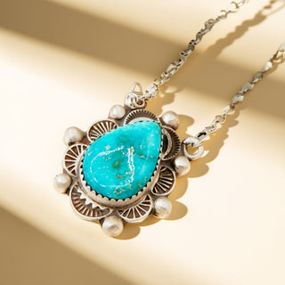 Necklace with turquoise stone and pearl accents on a beige background