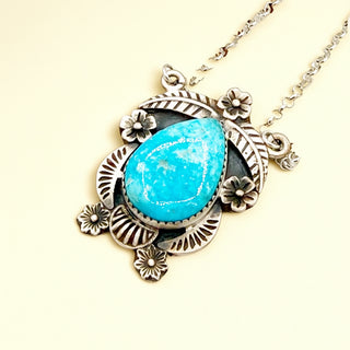 Necklace with a turquoise stone and silver floral design on a light yellow background